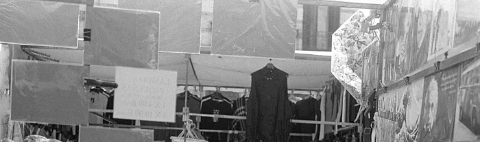 Ropa colgada y cuadros apoyados en un puesto de El Rastro de Madrid